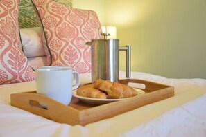 A tray with croissants, a coffee pot, and a cup on a bed with patterned pillows. - Seawall Cottage, Aldeburgh (Aldeburgh)