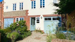 A two-story house with a brick facade, a blue garage door, and a front garden with various plants. - Seawall Cottage, Aldeburgh (Aldeburgh)