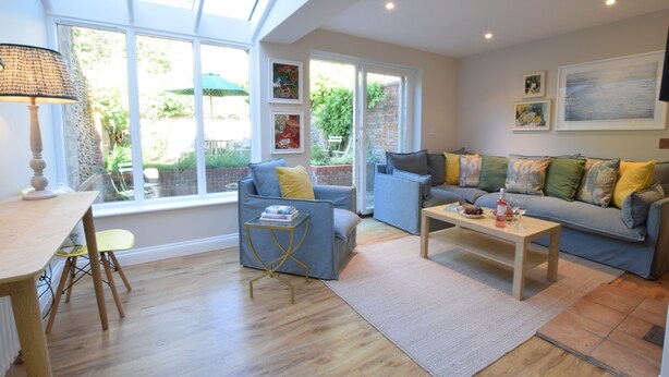 A spacious living room with a sofa, armchairs, a coffee table, and a dining table. There are large windows providing natural light and a view of the outdoors. - Seawall Cottage, Aldeburgh (Aldeburgh)