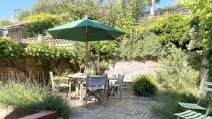 An outdoor patio with a table and chairs, a green umbrella, and a brick wall. - Seawall Cottage, Aldeburgh (Aldeburgh)
