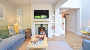 A living room with a sofa, coffee table, fireplace, television, and bookshelves. - Seawall Cottage, Aldeburgh (Aldeburgh)