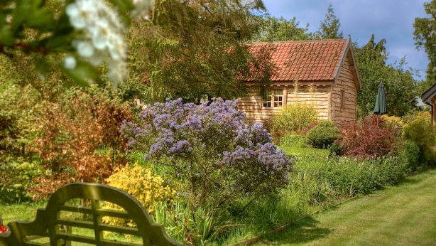 Una cabaña rústica de troncos rodeada por un jardín exuberante con diversas plantas y flores.