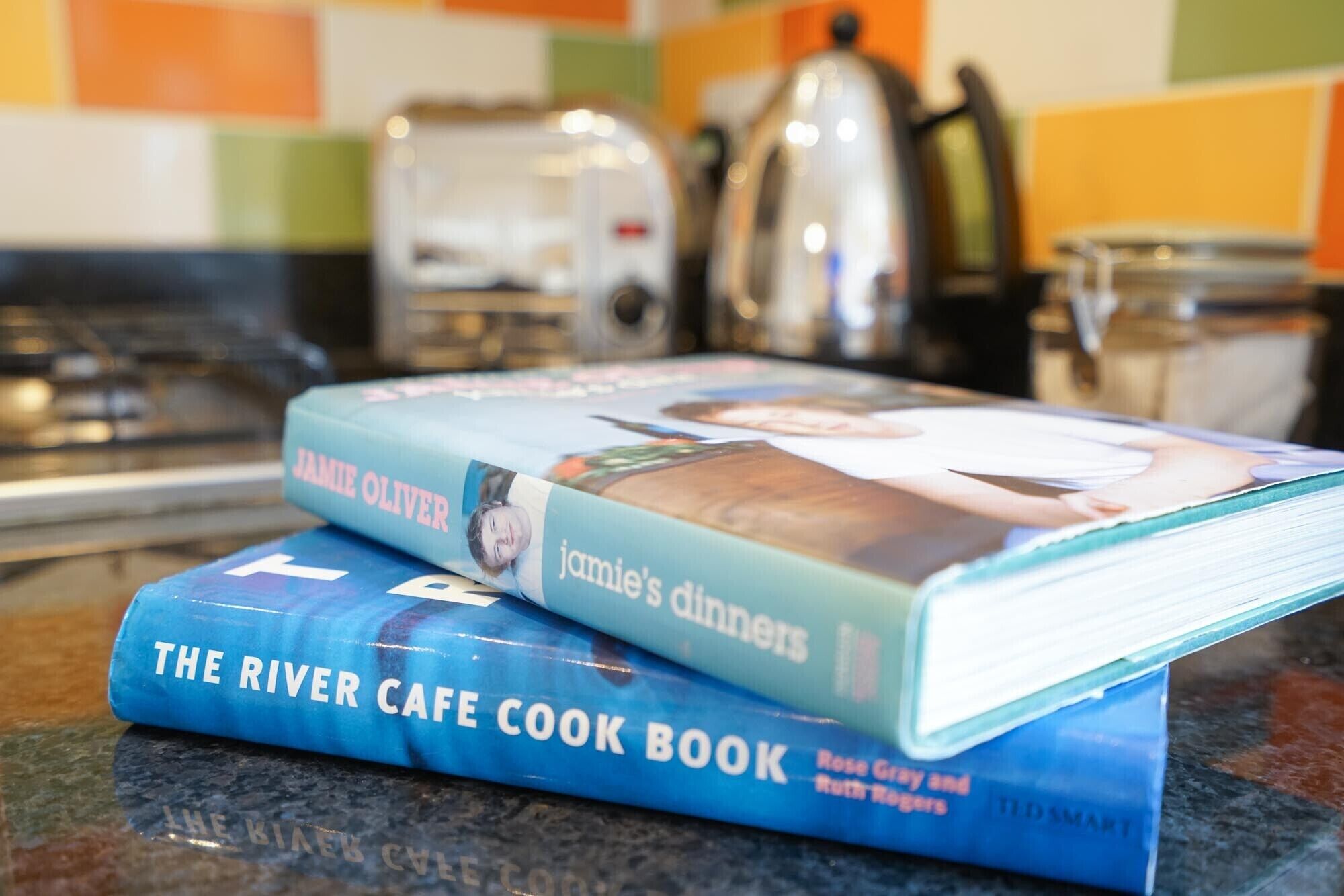 Zwei Kochbücher, 'Jamie Olivers Dinners' und 'The River Cafe Cook Book', auf einer Küchenarbeitsplatte.