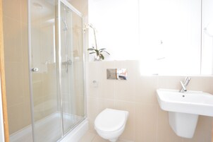 Un baño con ducha de vidrio, inodoro blanco y lavamanos.