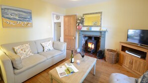 A living room with a sofa, coffee table, fireplace, television, and artwork. - Pebble Beach Cottage, Aldeburgh (Aldeburgh)