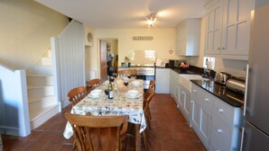 A kitchen with a dining table set for four, white cabinets, and a staircase leading to another level. - Pebble Beach Cottage, Aldeburgh (Aldeburgh)