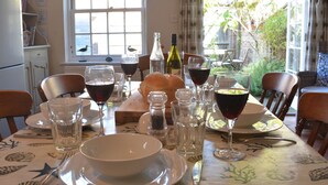 A dining table set with wine glasses, a bottle of wine, salt and pepper shakers, and a loaf of bread. - Pebble Beach Cottage, Aldeburgh (Aldeburgh)
