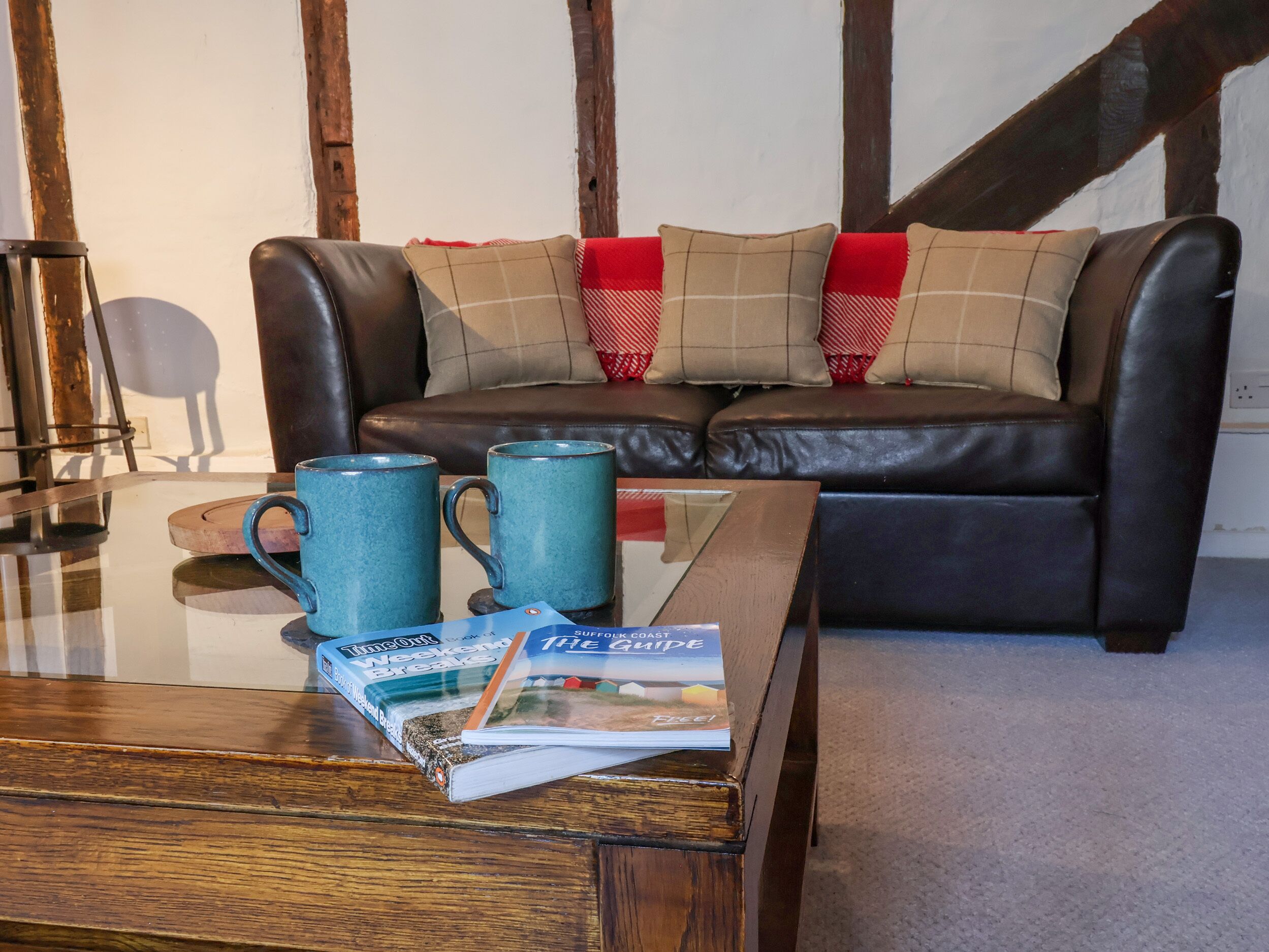 A living room with a glass coffee table, two blue mugs, a magazine, and a sofa with red and beige cushions.