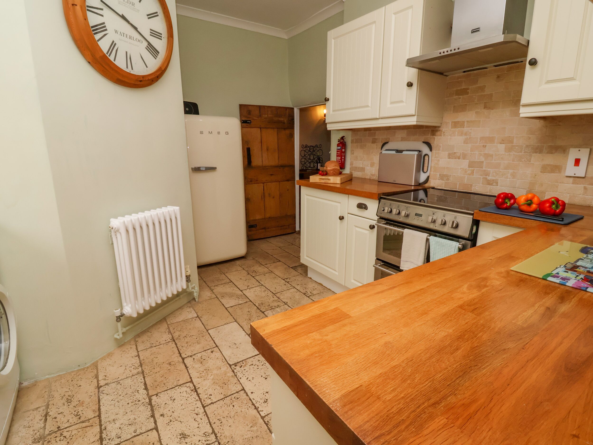A kitchen with white cabinets, a wooden countertop, a stove, and a clock on the wall.