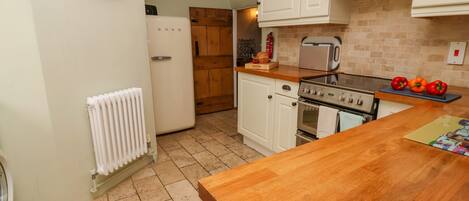 A kitchen with white cabinets, a wooden countertop, a stove, and a clock on the wall.