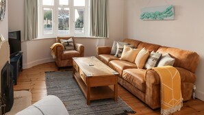 A living room with a brown leather sofa, a wooden coffee table, and a television on a stand.