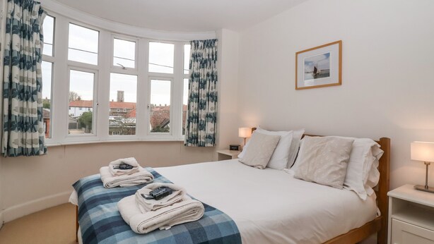 A bedroom with a large bed, two bedside tables with lamps, a framed picture on the wall, and a view of buildings through the windows.