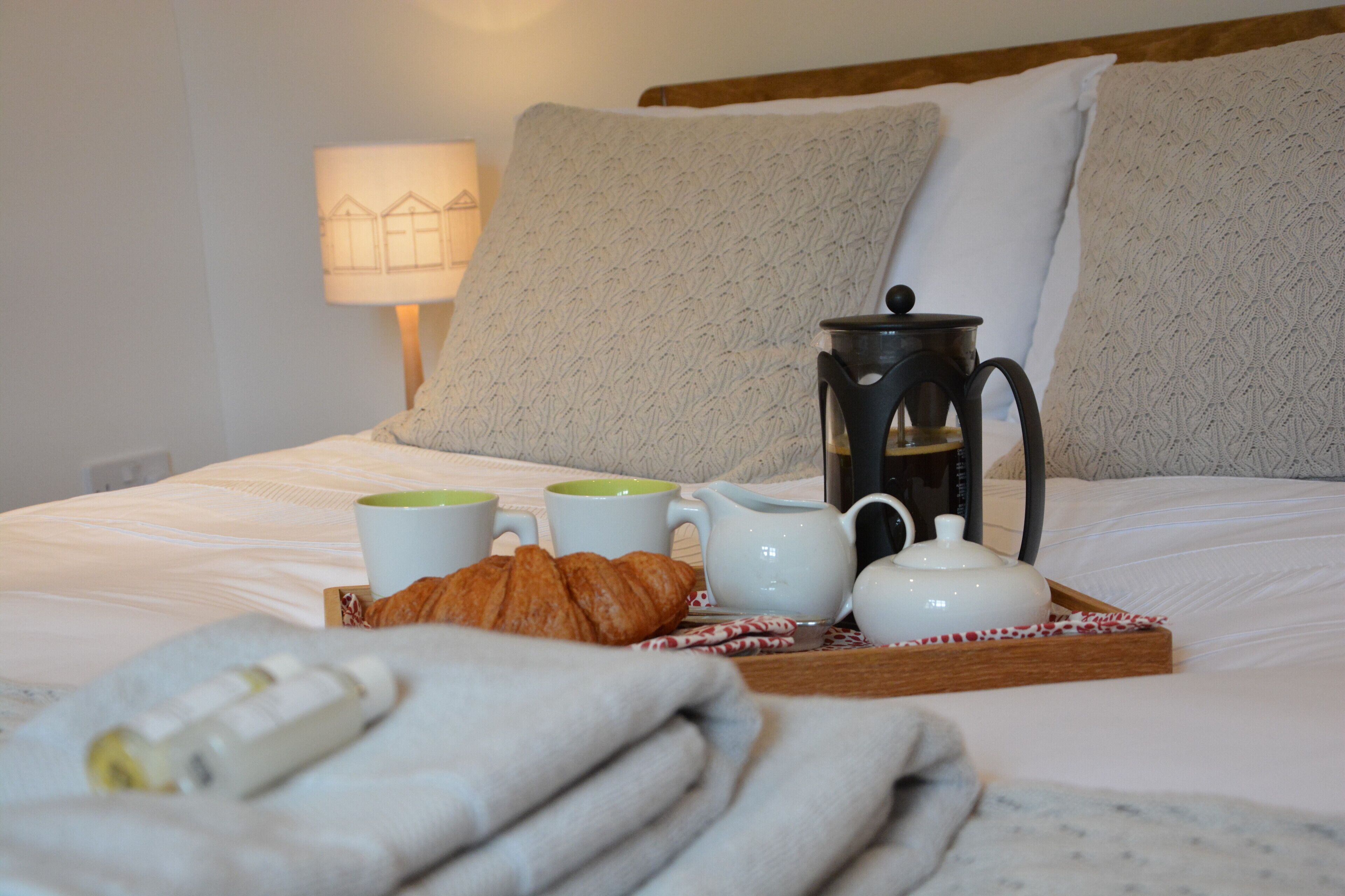 A neatly made bed with a tray of croissants, a teapot, and two cups, suggesting a breakfast setup in a hotel room.