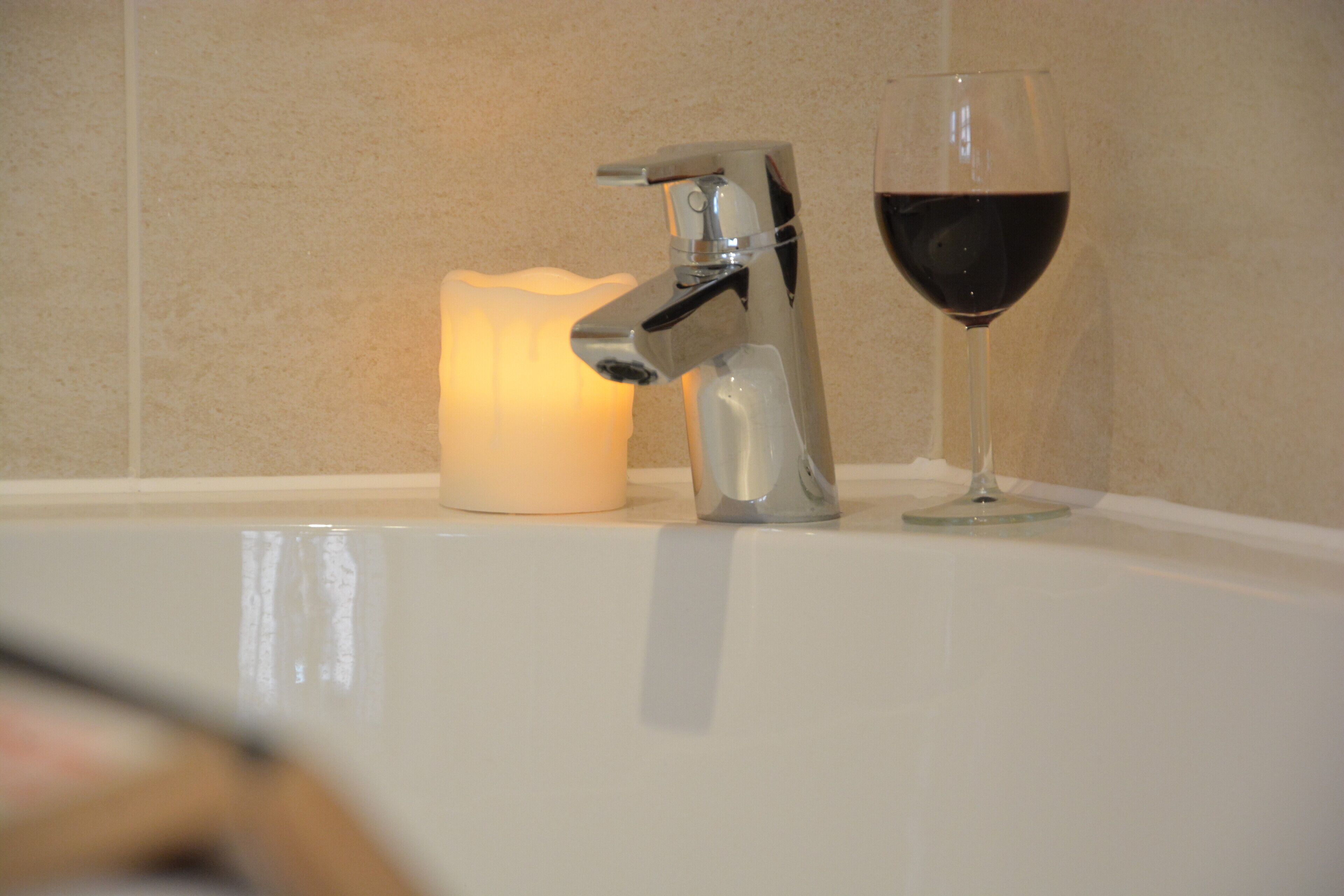A bathroom sink with a modern faucet and a glass of red wine.