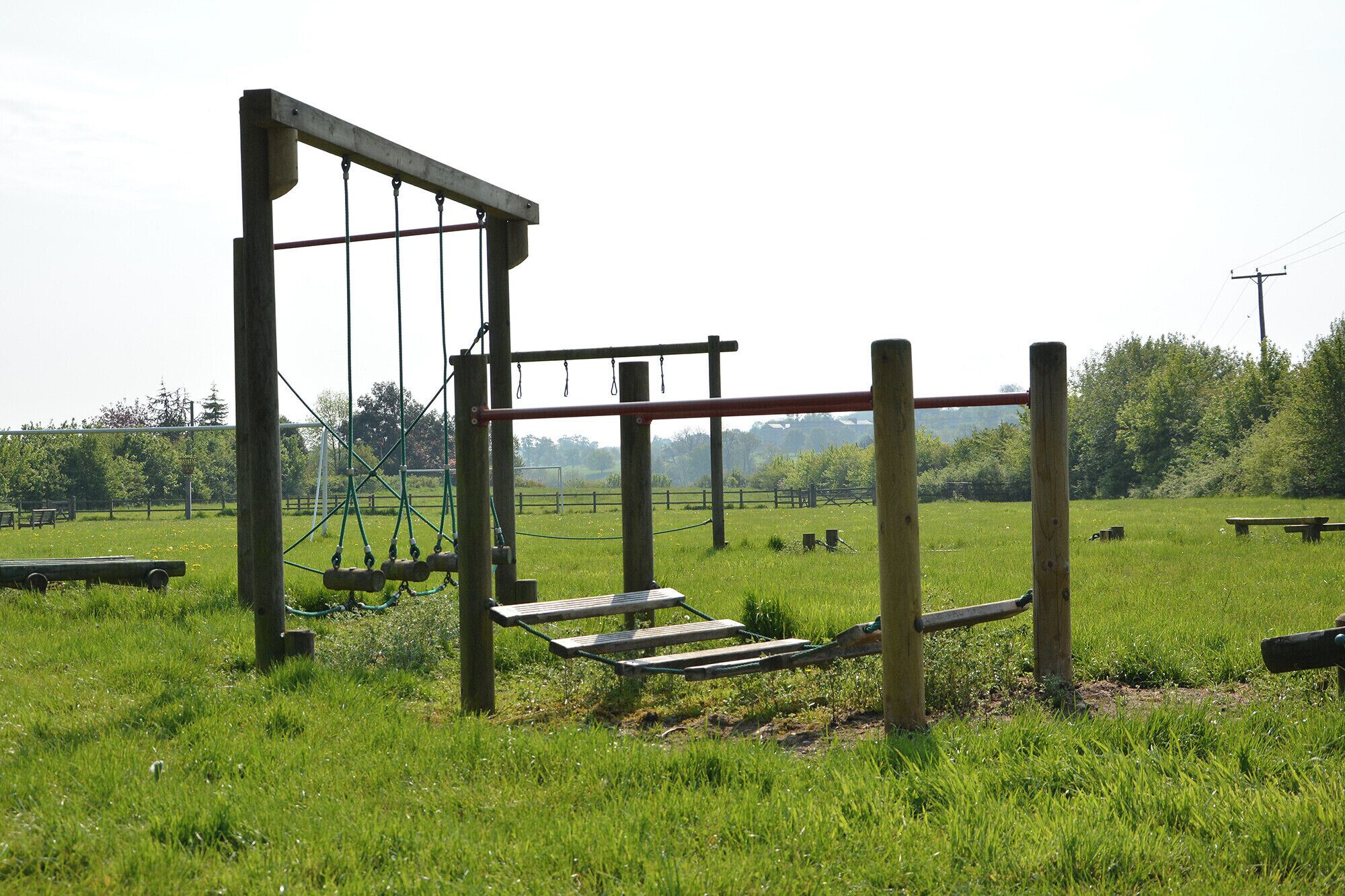 Un parque infantil con estructuras de madera y una mesa de picnic en un campo cubierto de césped.