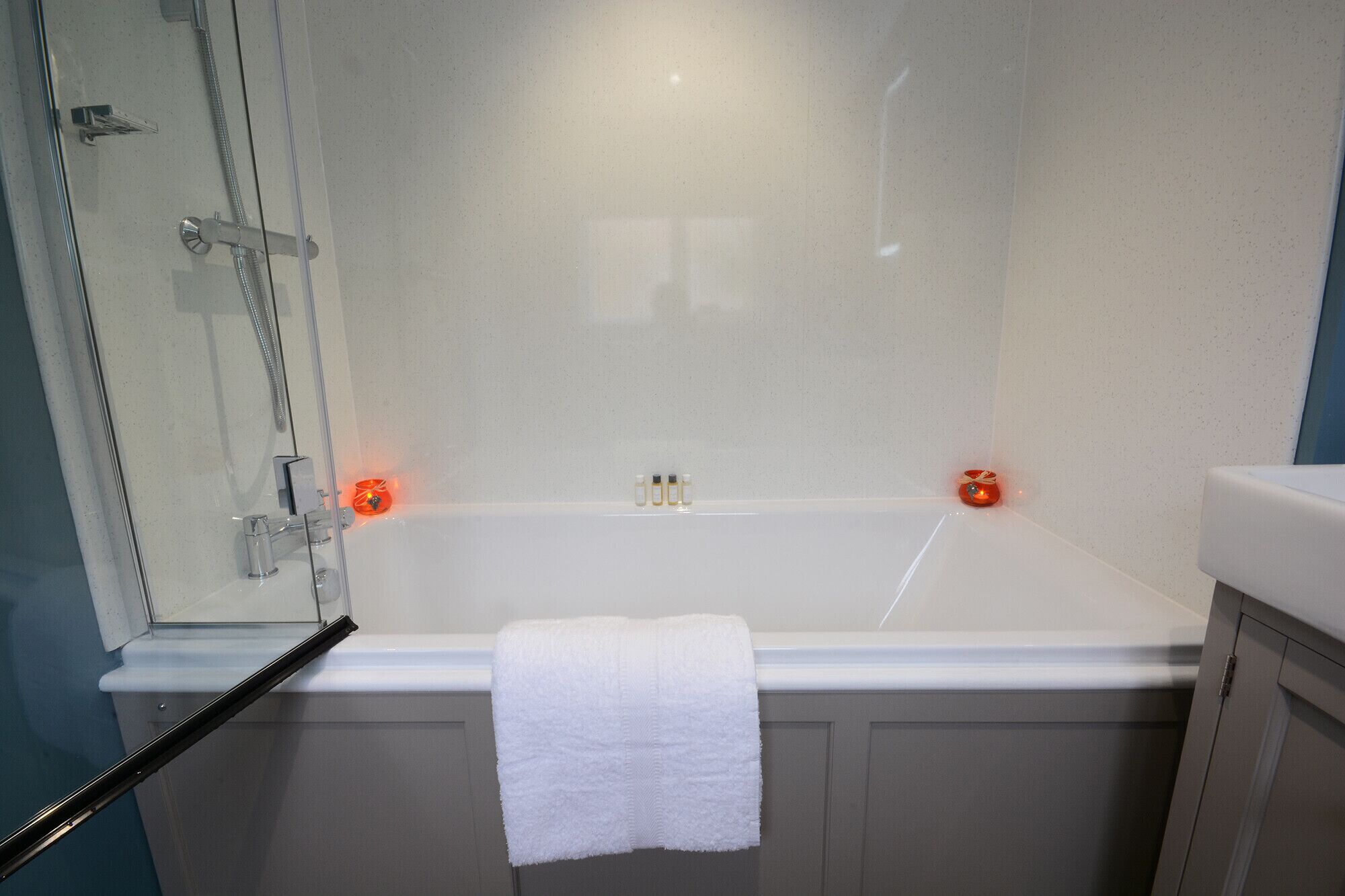 Ein Badezimmer mit einer weißen Badewanne, einer Duschkabine aus Glas und einem weißen Handtuch an der Wand.