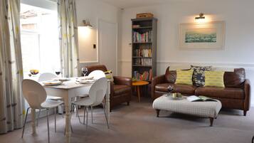 A dining area with a table set for two, a bookshelf, and a leather sofa with cushions.