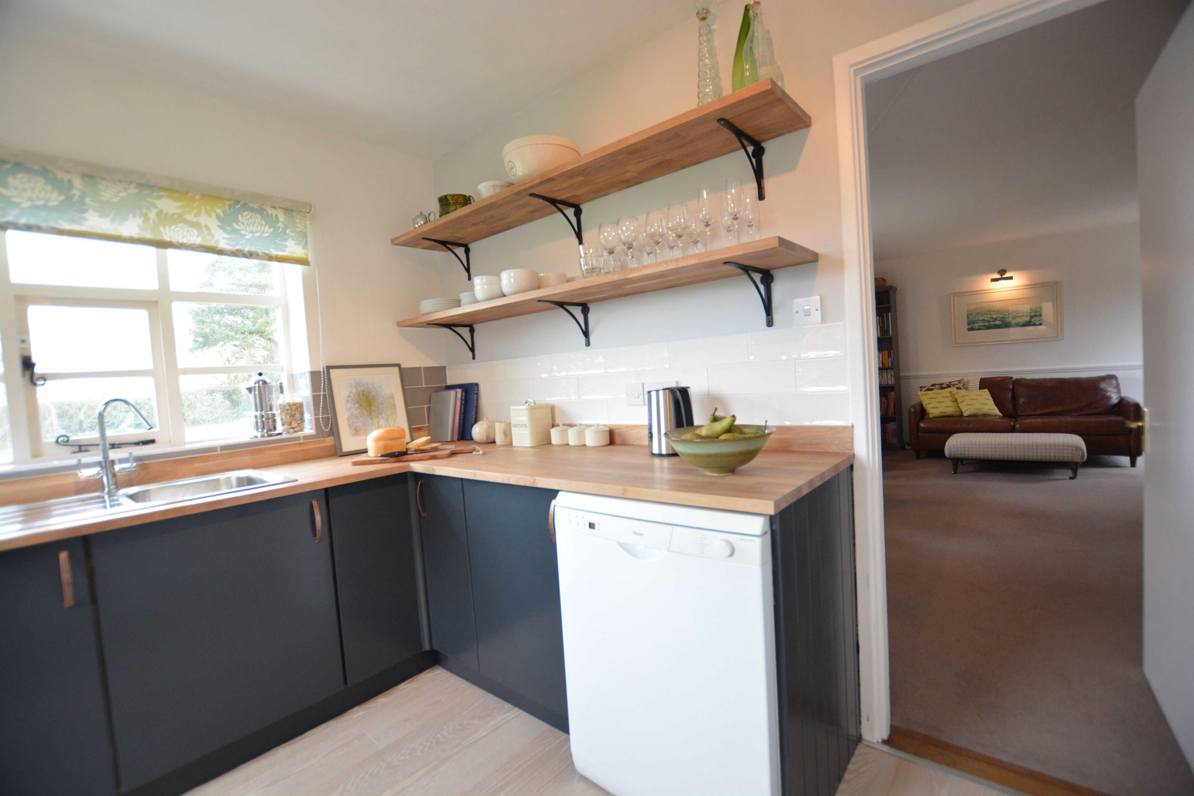Una cucina moderna con mobili scuri, una lavastoviglie ed scaffali in legno con piatti e bicchieri.
