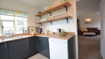 Una cucina moderna con mobili scuri, una lavastoviglie ed scaffali in legno con piatti e bicchieri.