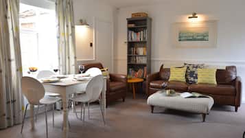 A dining area with a table set for two, a bookshelf, and a leather sofa with cushions.