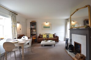 A living room with a fireplace, a dining table with chairs, a sofa, a bookshelf, and a large mirror. - Rookyards (Halesworth)