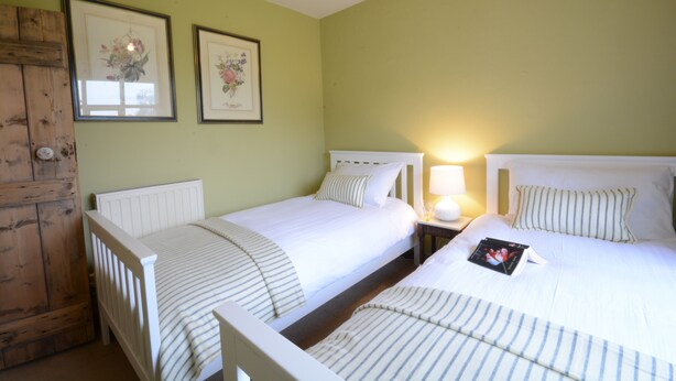 A hotel room with two beds, a wooden door, and two framed floral pictures on the wall. - Rookyards (Halesworth)