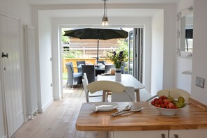 A dining area with a wooden table, chairs, and a bowl of fruit. - 4 The Dunes, Thorpeness (Leiston)