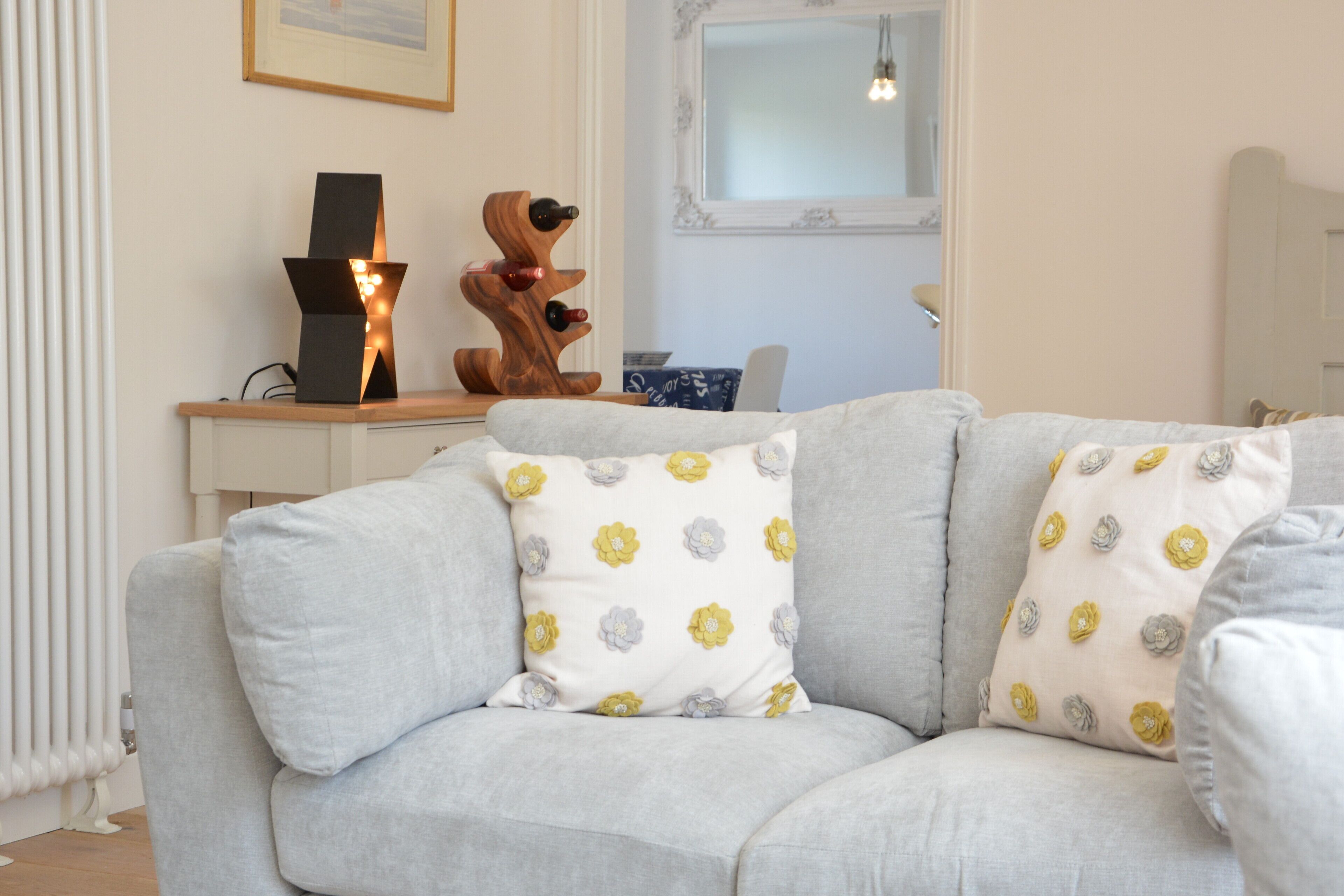A modern living room with a grey sofa, floral patterned cushions, a wooden sculpture, and a framed picture on the wall.