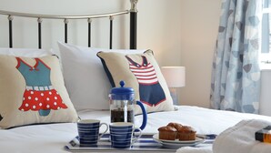 Cama bem arrumada com almofadas decorativas, uma cafeteira e uma bandeja com muffin e xícaras de café.