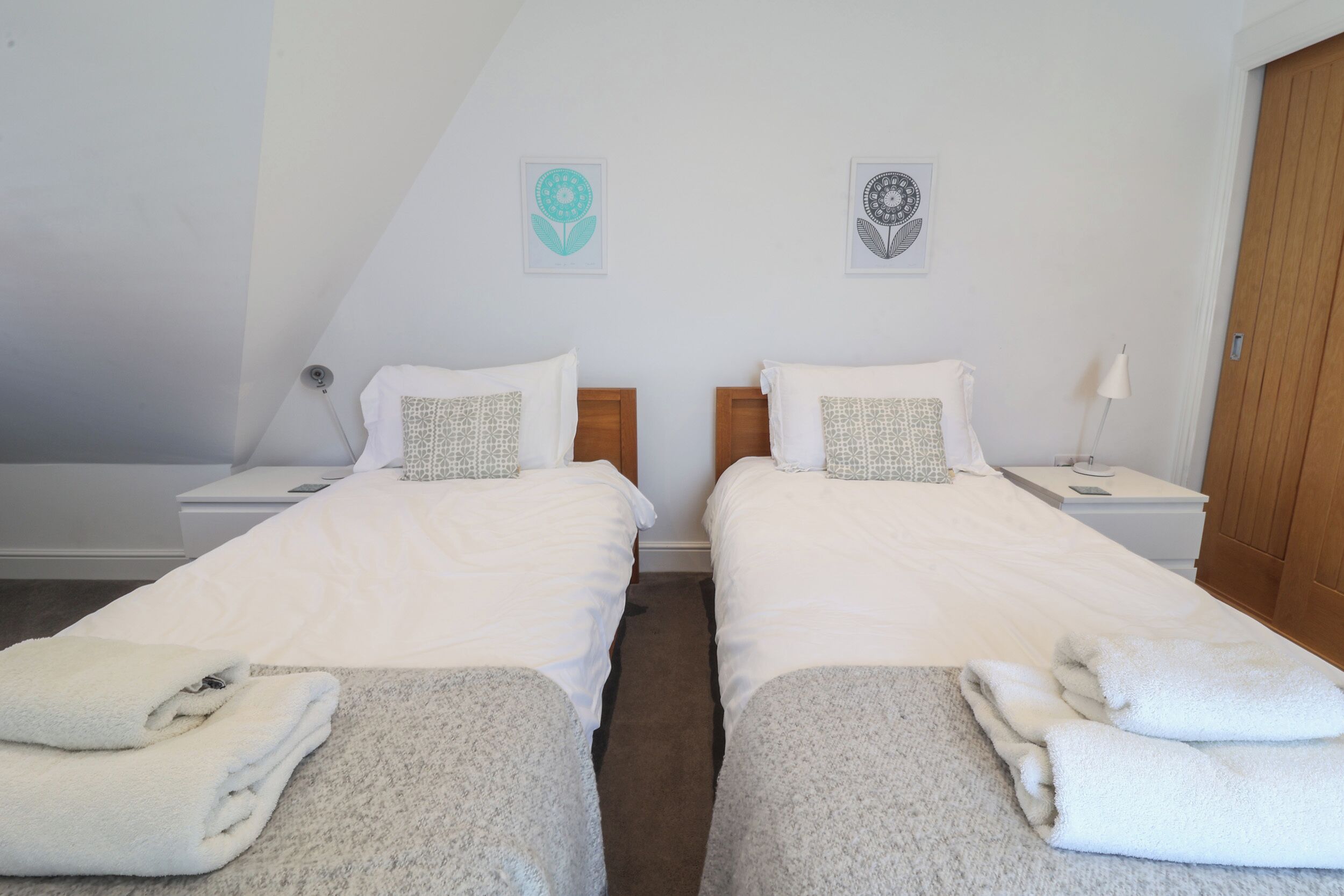 Une chambre double avec deux lits, une armoire en bois, une table de chevet avec une lampe et une œuvre d’art accrochée au mur.