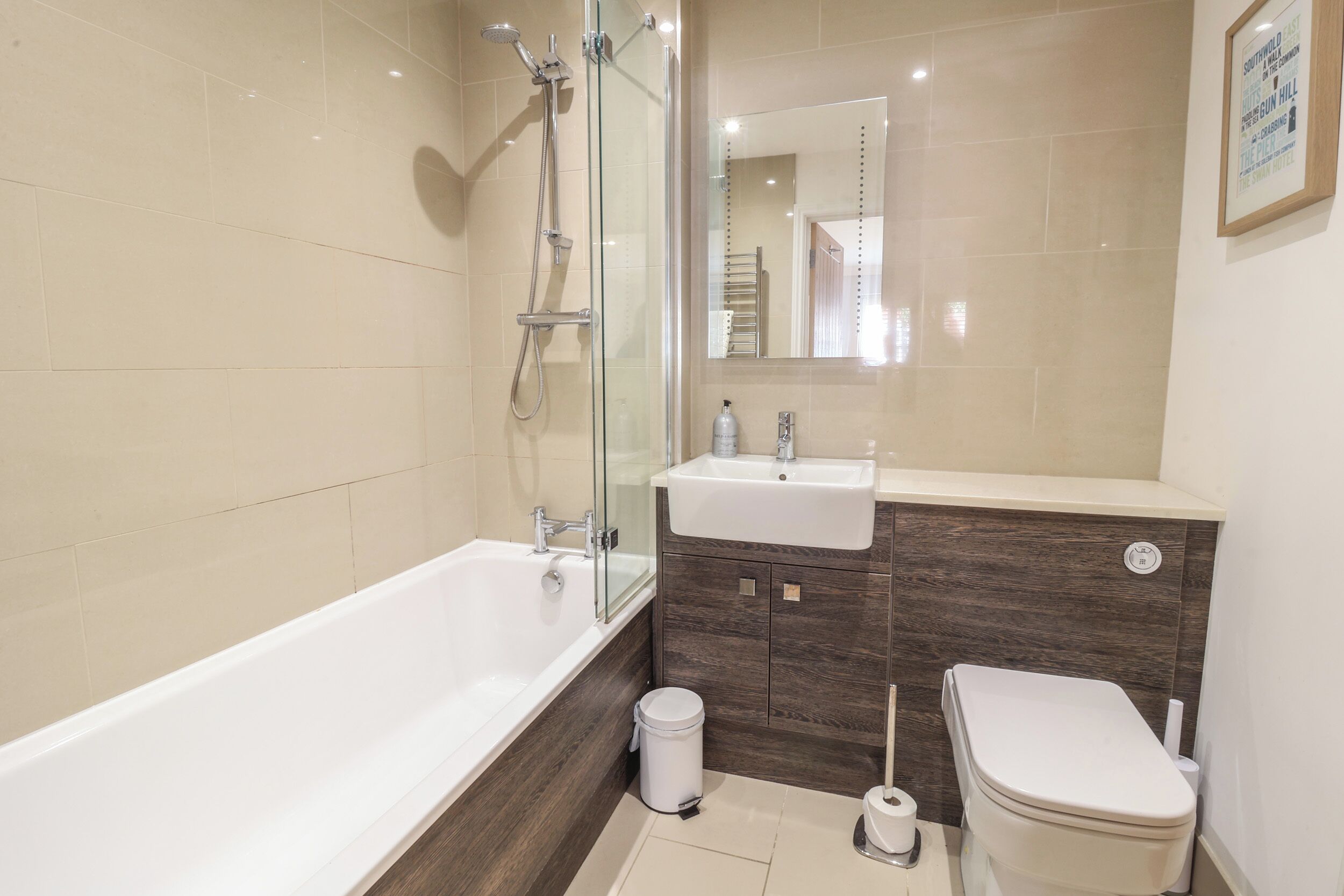 A modern bathroom with a glass-enclosed shower, a white bathtub, a wooden vanity with a sink, and a toilet.