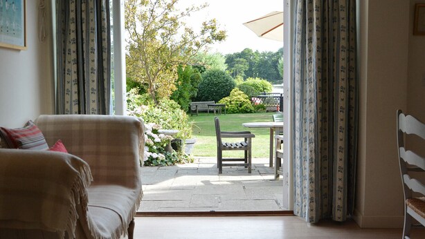 Une pièce comprenant un canapé, une table à manger et une chaise. On peut admirer, depuis cette pièce, un jardin avec un banc et une table situés à l’extérieur.