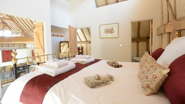 A bedroom with a large bed, a wooden ceiling, a mirror, and a framed picture on the wall.