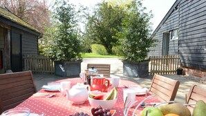An outdoor dining area with a red tablecloth, various fruits, and a wooden fence in the background.