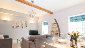 Un salon moderne avec un canapé gris, une table à manger en bois dressée pour deux personnes et un téléviseur en arrière-plan.
