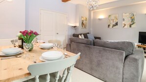 Un coin repas avec une table en bois dressée pour deux personnes, un canapé gris et un lustre.
