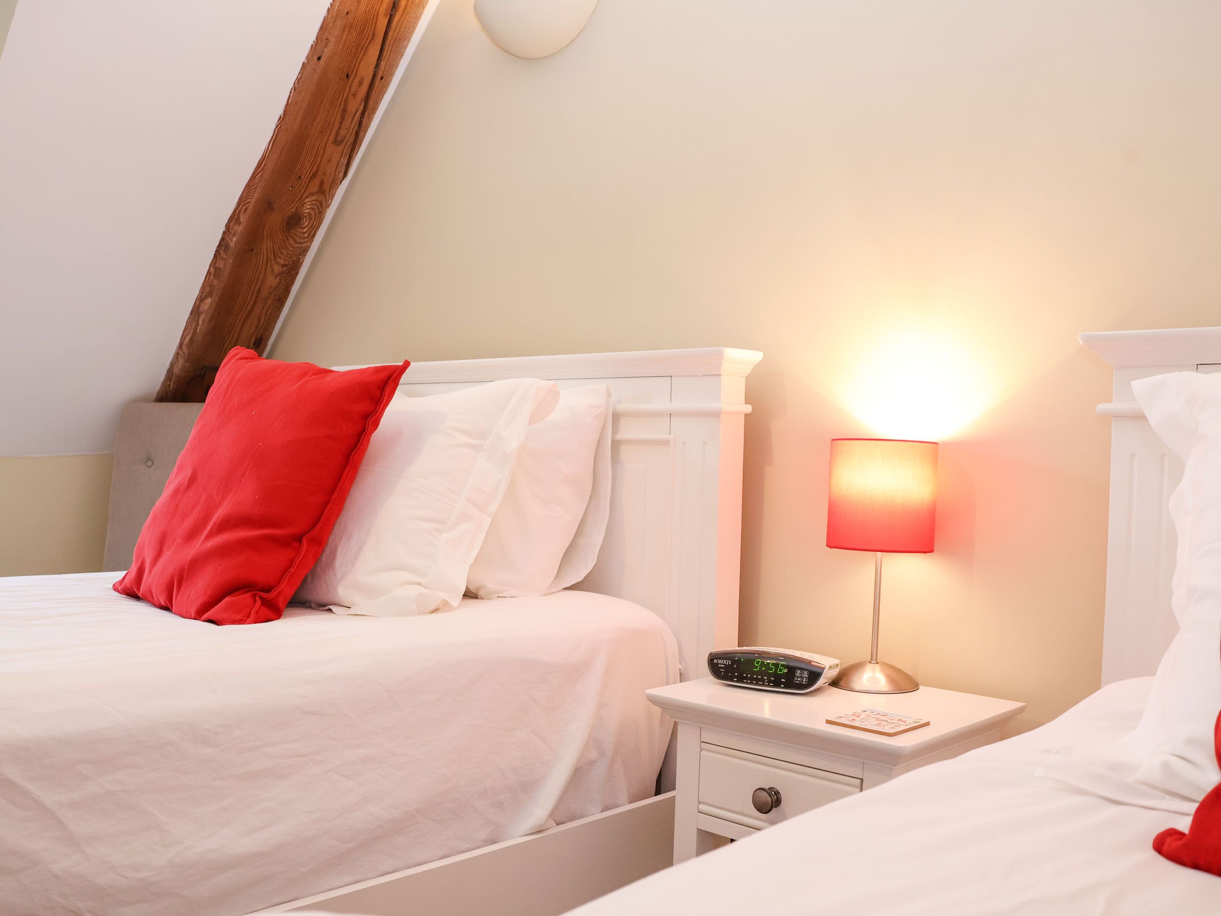 A bedroom with two beds, a nightstand with a lamp, and a wall clock.