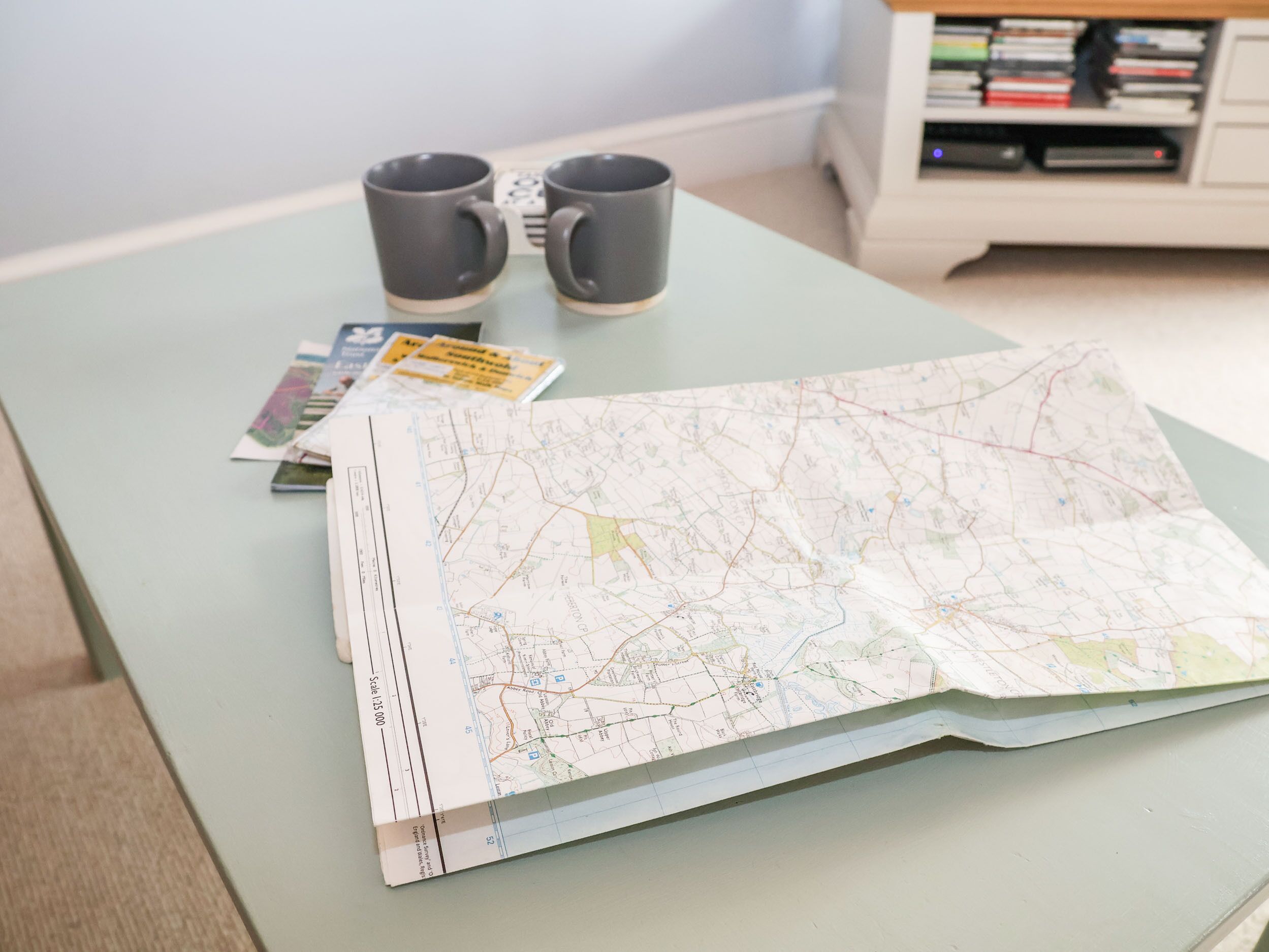 A map spread on a table with two mugs and a book.