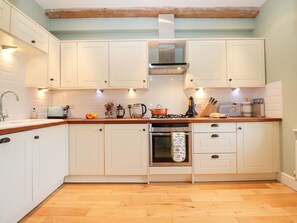 A kitchen with white cabinets, a wooden countertop, a stove, an oven, and a sink. - Saffron, Blythview (Halesworth)