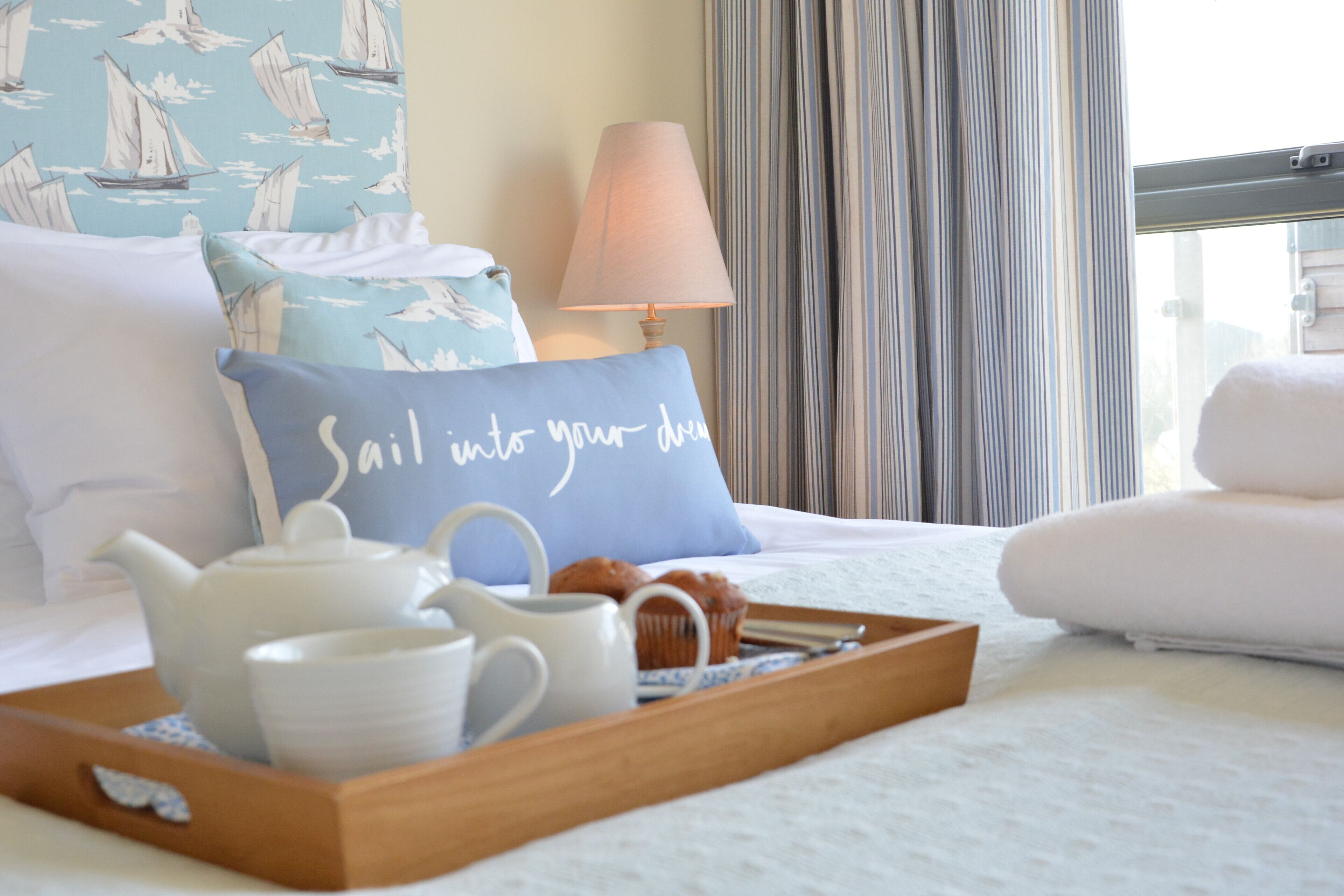 Una cama bien hecha con una bandeja de desayuno, una tetera y una almohada con motivos náuticos.