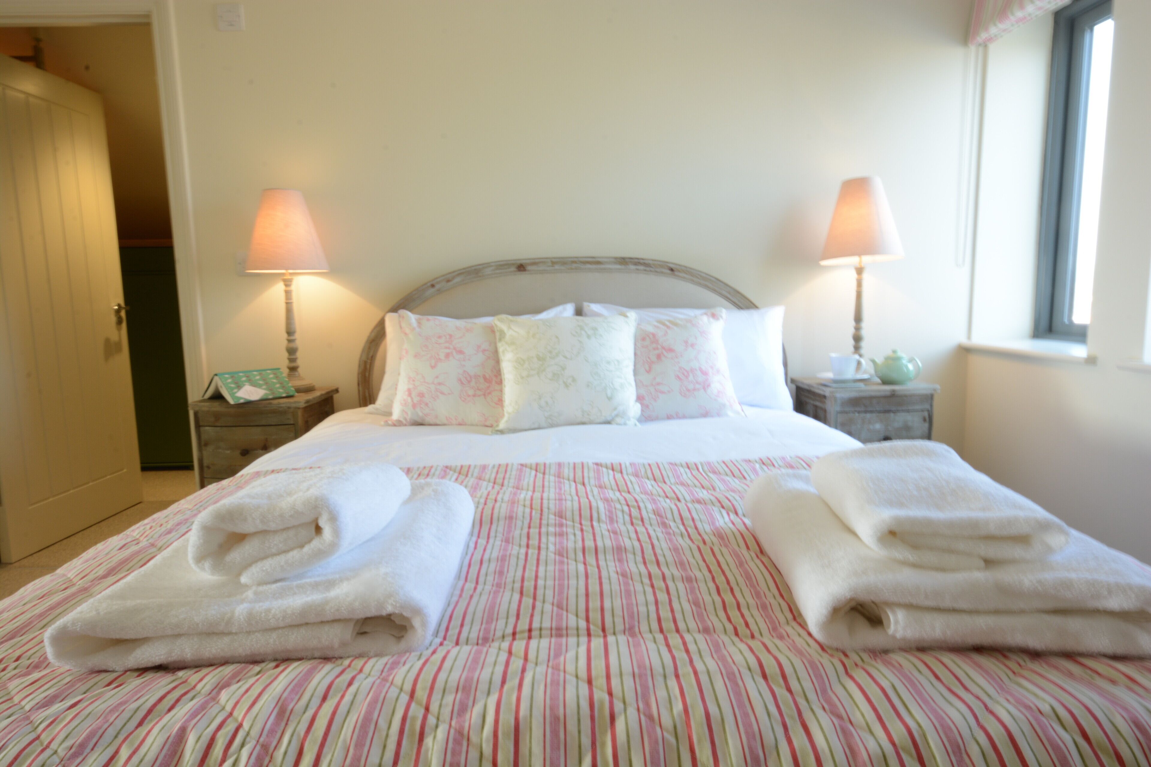 A neatly made bed with striped bedding, two bedside lamps, and a window with a view.