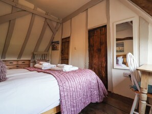 A bedroom with a bed, a wooden chair, a wooden door, and a window. - Pudding Cottage, Westleton (Saxmundham)