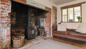 A cozy room with a brick fireplace, a brown leather sofa, and a wicker basket. - Pudding Cottage, Westleton (Saxmundham)