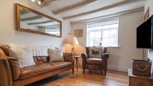 A cozy living room with a brown leather sofa, a wooden armchair, a large mirror, and a wooden cabinet with a handle. - Pudding Cottage, Westleton (Saxmundham)