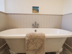 A bathroom with a freestanding bathtub, a small framed picture on the wall, and patterned floor tiles. - Pudding Cottage, Westleton (Saxmundham)