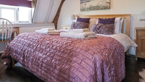A bedroom with a wooden ceiling, a bed with a pink quilt, and a painting above the bed.