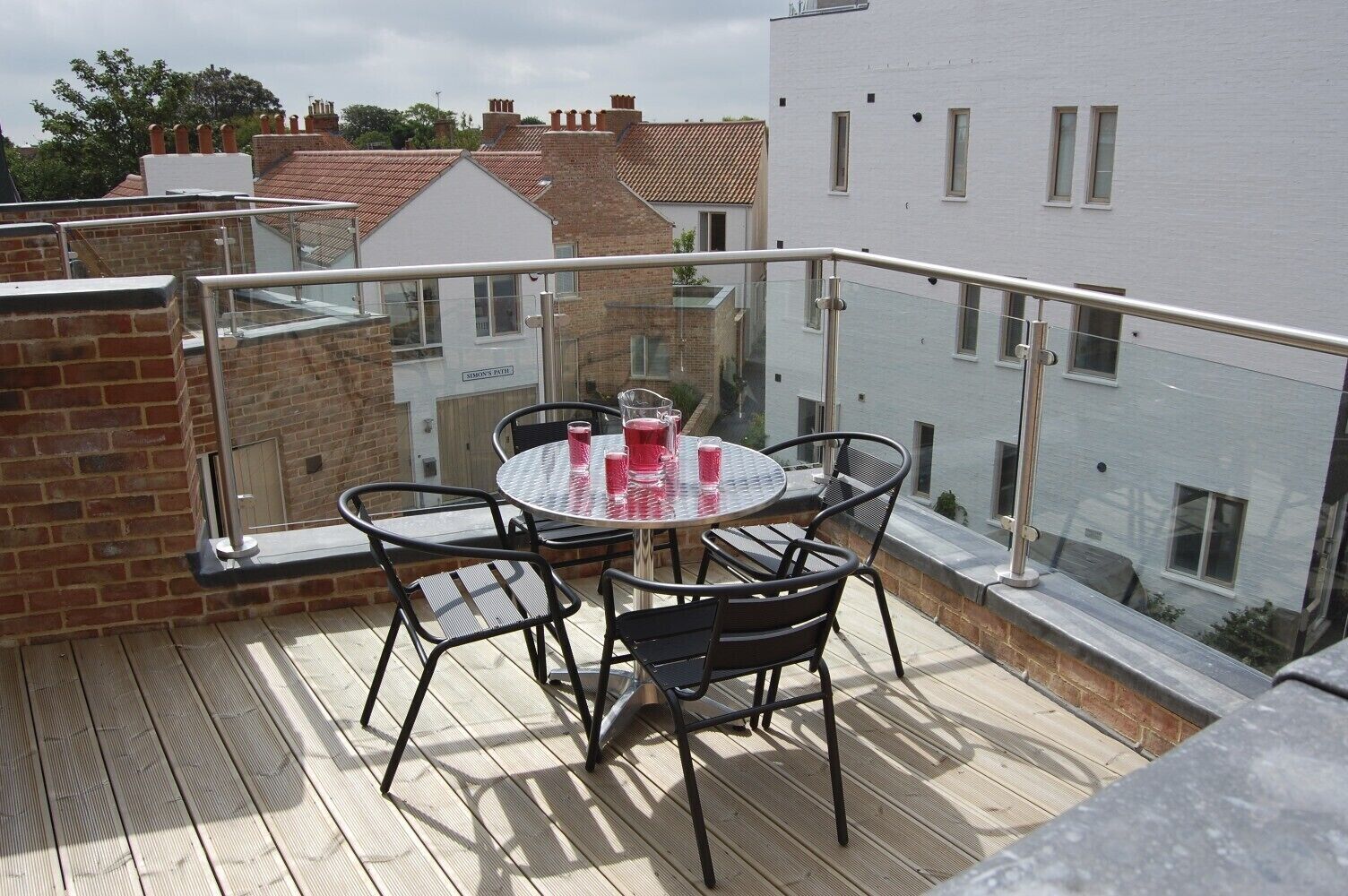 Un balcon avec une table ronde et des chaises, une balustrade en verre et une vue sur les immeubles voisins.