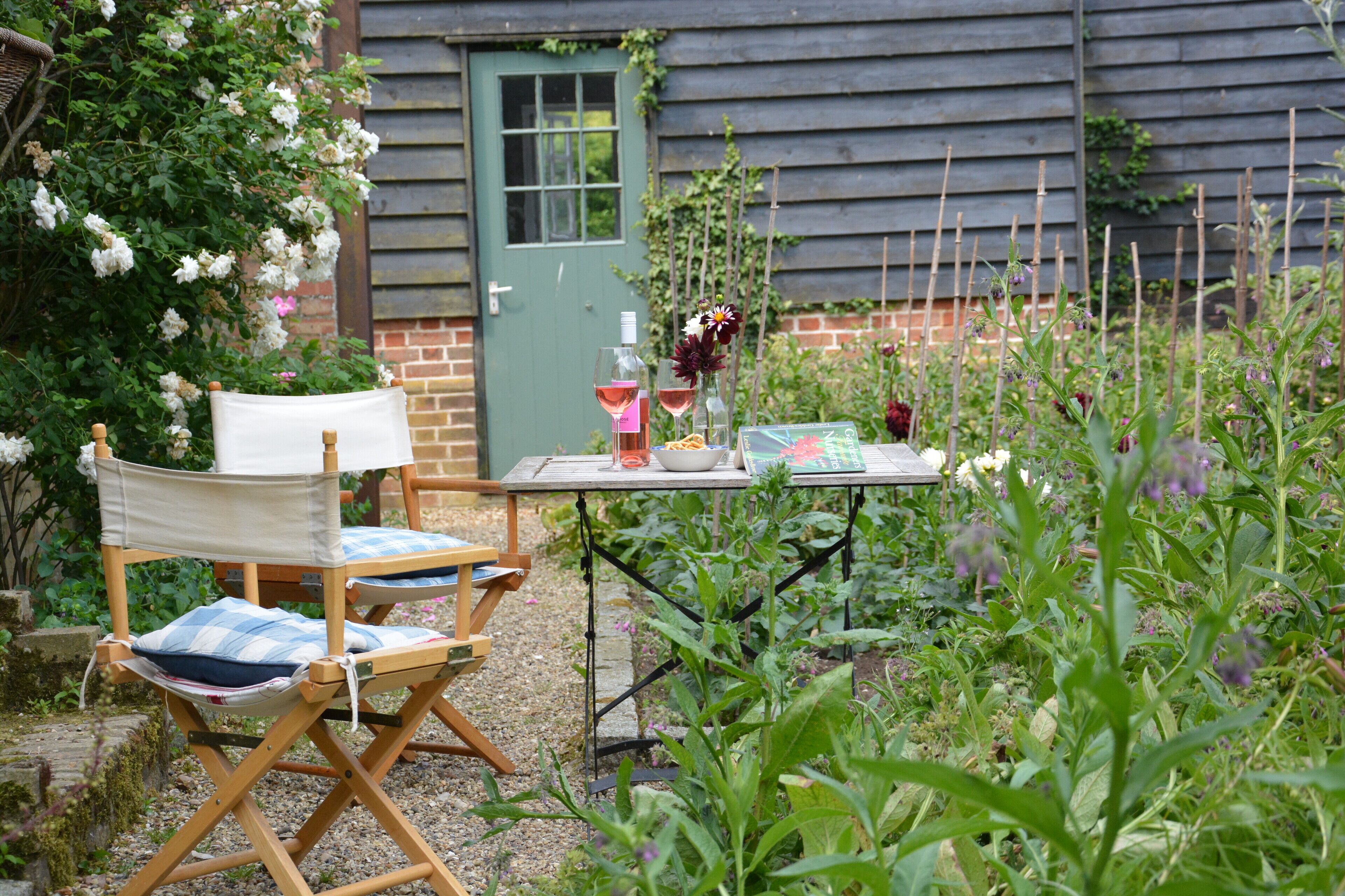 A garden with a table set for two, surrounded by plants and a wooden chair.