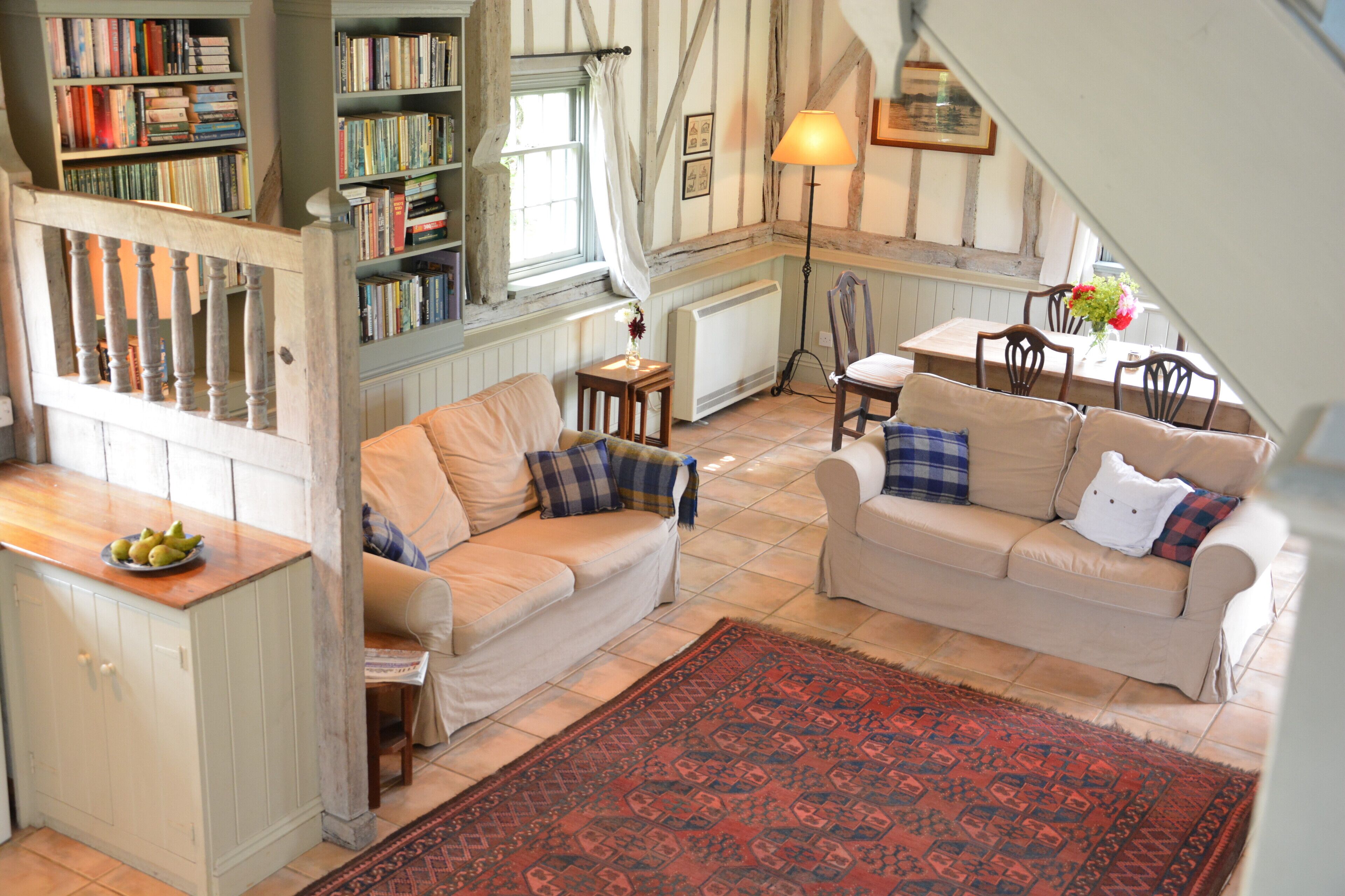 A cozy living room with two beige sofas, a red patterned rug, and a bookshelf filled with books.