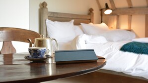 Ein Holztisch mit Teekanne, Tasse und Buch in einem Zimmer mit Bett und weißer Bettwäsche.